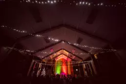 Candlelit Christmas carol service at St Columba’s Derryvolgie with festive lights across the ceiling, colourful lighting on the altar, and the congregation gathered in worship.