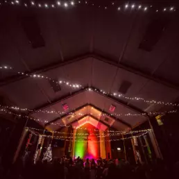Candlelit Christmas carol service at St Columba’s Derryvolgie with festive lights across the ceiling, colourful lighting on the altar, and the congregation gathered in worship.