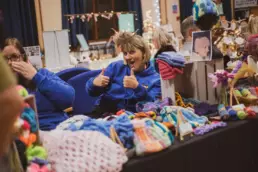 Smiling stallholder giving a thumbs-up behind a table of colourful knitted crafts at the Twilight Market