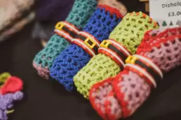 Festive crocheted dishcloths tied with decorative belts at a handmade crafts stall
